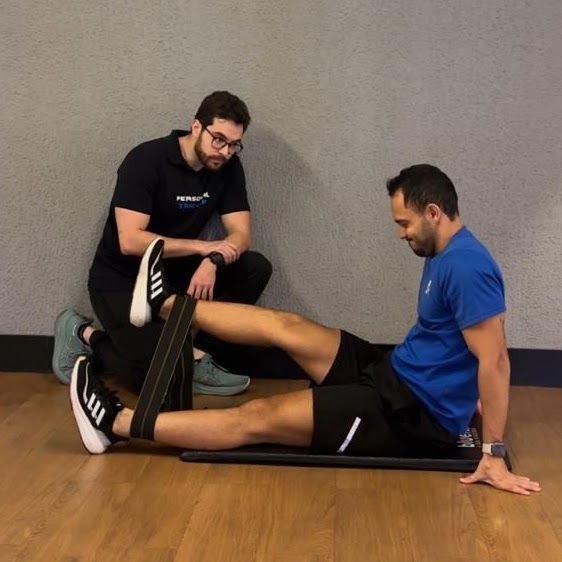 Barbosa acompanha um aluno em um exercício com elástico no chão da academia